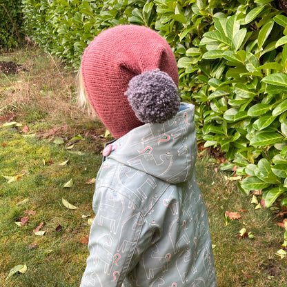 a simple pixie hat knitting pattern. photo shows the rear view of a child wearing a rust coloured hat 