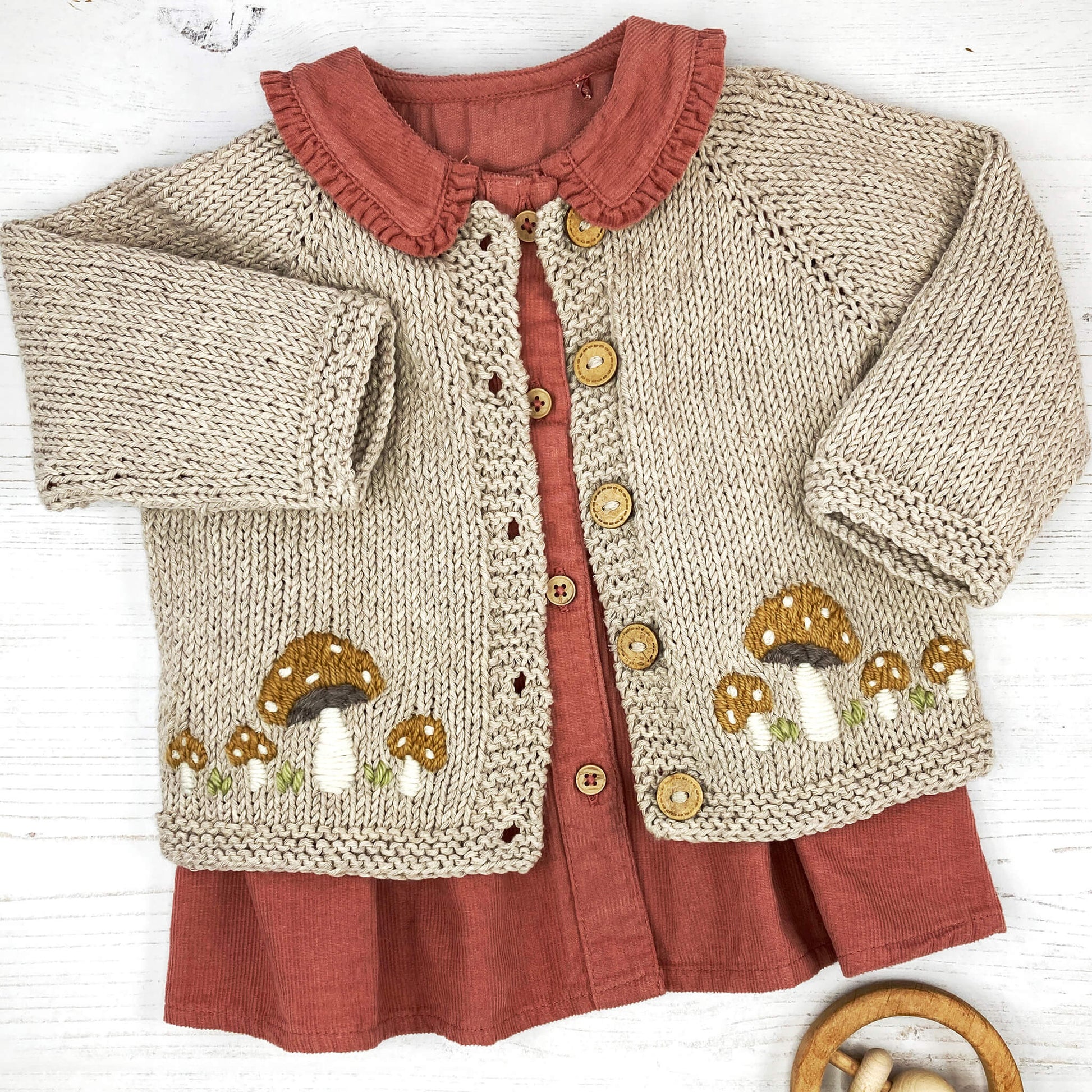 a cardigan knitting pattern with toadstool embroidery shown over a rust coloured top