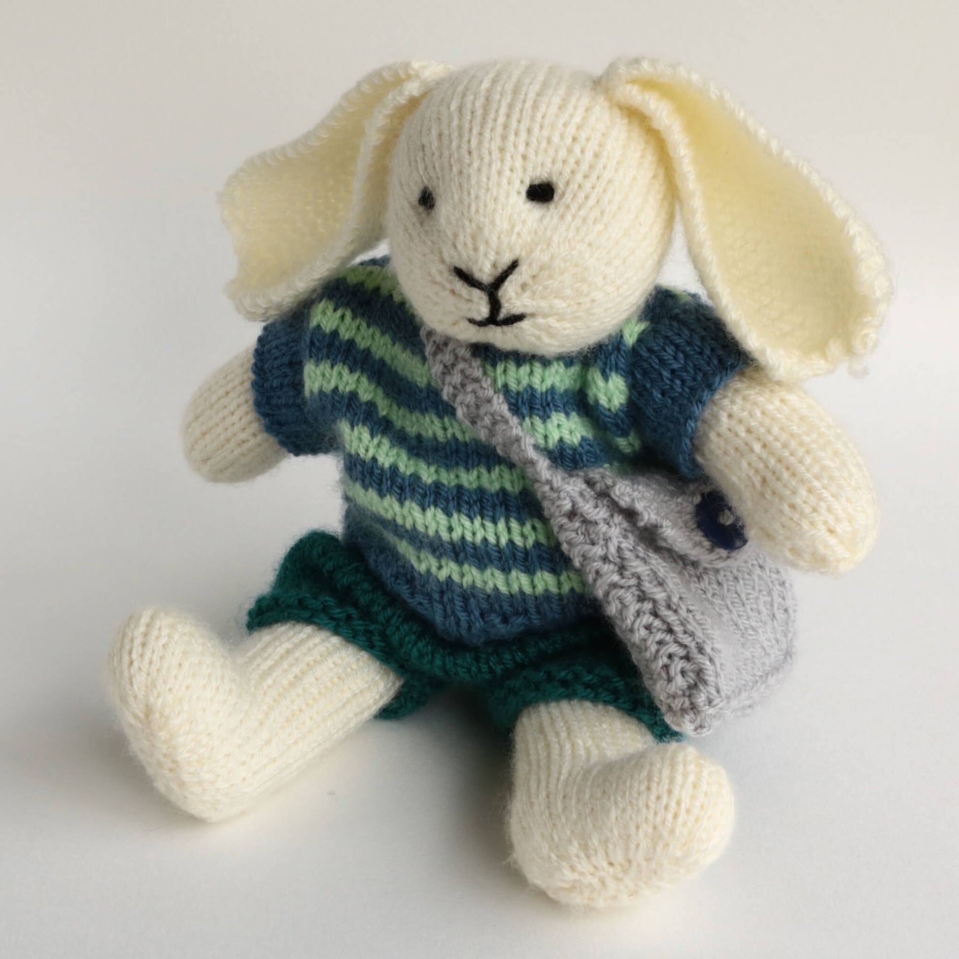 a toy rabbit knitting pattern. the rabbit shown is sitting dressed in a striped top and shorts